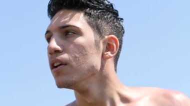 Denizdeki çekici genç adam ıslak saçlarıyla sudan çıkıyor, etrafa bakıyor ve saçlarına dokunuyor.