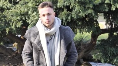 One handsome blue eyed young man sitting on bench in urban setting in European city park