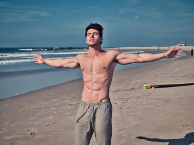 Muscular young man on the beach, with arms open enjoying the sensation of freedom in front of the sea or ocean