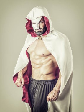 Serious strong male with naked muscular torso dressed in vintage style cape, wearing white half mask, looking at camera with challenge