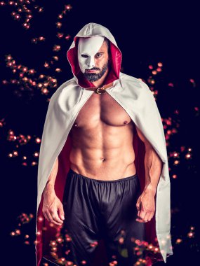 Serious strong male with naked muscular torso dressed in vintage style cape, wearing white half mask, looking at camera with challenge