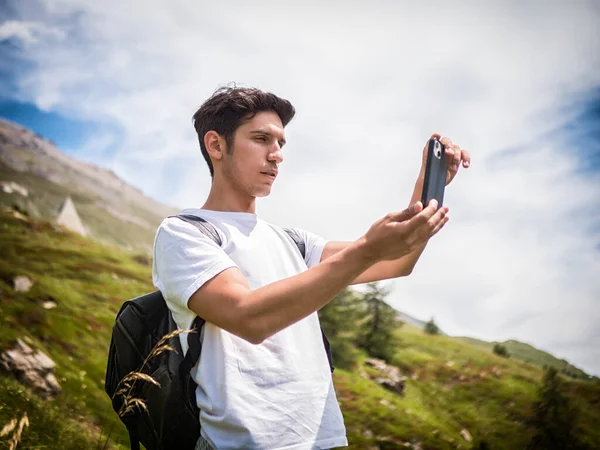 Young Attractive Man Taking Photo With Cell Phone Up in the Mountains, with Back Pack