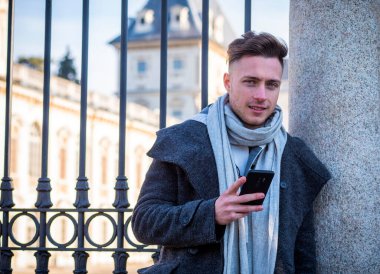 Trendy yakışıklı cardingan ayakta ve cep telefonuyla, açık şehir ayarında gün atış yazarak