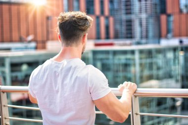 Handsome fit man in white t-shirt outdoor in city setting, seen from the back