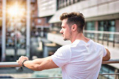 Handsome fit man in white t-shirt outdoor in city setting, seen from the back