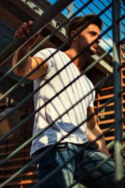 Handsome fit man in white t-shirt outdoor in city setting, climbing metal stairs, looking away