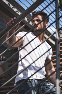 Handsome fit man in white t-shirt outdoor in city setting, climbing metal stairs, looking away