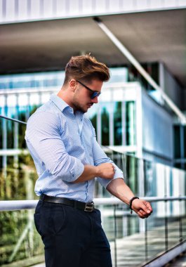 One handsome elegant man in urban setting in European city, standing, rolling up shirts sleeves