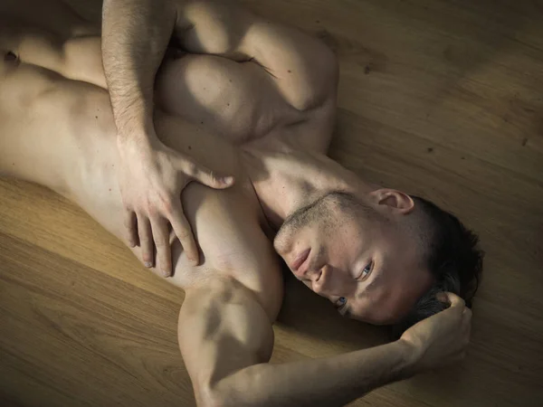ハンサムな全裸筋肉青年魅惑的な態度で自宅に堅木張りの床の敷設カメラ目線 — ストック写真