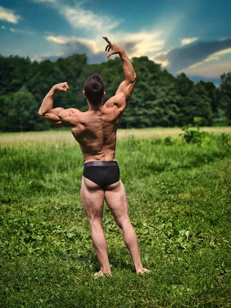 筋肉のシャツレスの若いハンクマン屋外の草の上に立っている 外を見ながら健康な筋肉体を表示する — ストック写真