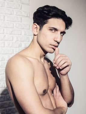 Yakışıklı bir delikanlının yüzü beyaz duvara karşı, eli çenesinde, kameraya yandan bakıyor.