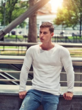 Şehirde beyaz gömlek ve kot pantolon giyen kaslı genç adam.