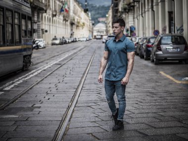 Yakışıklı, kaslı, genç bir adam şehrin dışında dikiliyor ve sokağın ortasına bakıyor.