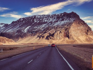 Modern araba İzlanda gezisi sırasında asfalt kırsal yolda muhteşem karlı dağlara doğru gidiyor.