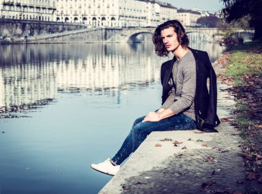 Avrupa şehrinde yakışıklı bir genç adam, Torino, İtalya 'da Po nehrinin kıyısında oturuyor, soğuk kış gününde.