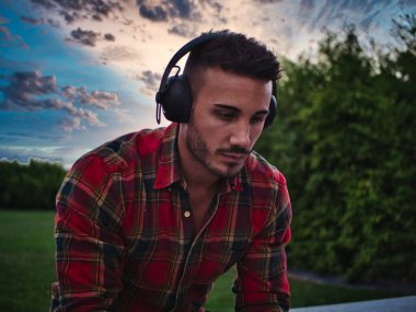 Şehirde genç ve çekici bir adam. Kulaklıkla müzik dinliyor, bankta oturuyor.