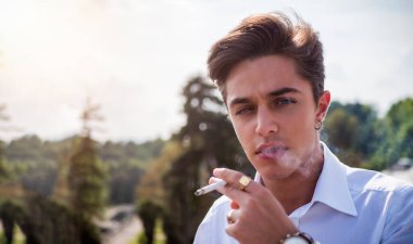 Avrupa 'nın şehir merkezinde sigara içen yakışıklı, zarif bir genç adam güneşli bir günde kameraya bakıyor.