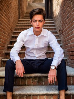 Avrupa 'da şehir ortamında yakışıklı, zarif bir genç adam eski merdivenlerde oturuyor ve kameraya bakıyor.