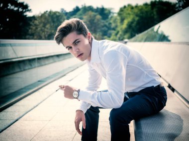 Yakışıklı bir genç adam Avrupa 'nın şehir merkezinde sigara içiyor güneşli bir günde oturuyor ve kameraya bakıyor.