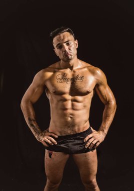 Üzgün, endişeli, kaslı, üstsüz genç adam ayakta kameraya bakıyor.