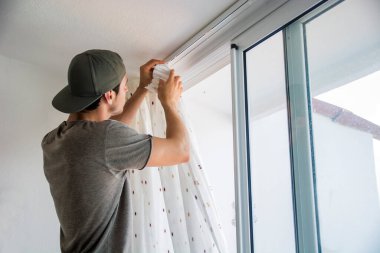 Genç yakışıklı bir adam ya da tamirci evdeki perdeleri takıyor, tadilat yapıyor.