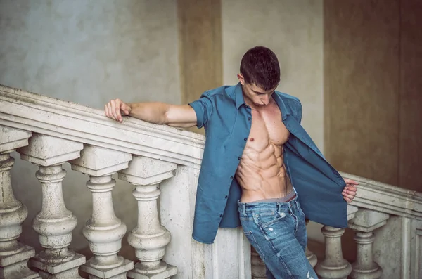 经典建筑内裸露躯干上开衬衫的迷人年轻肌肉男的画像 靠着抛光的大理石楼梯栏杆 — 图库照片