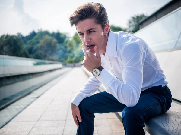 Avrupa 'nın şehir merkezinde sigara içen yakışıklı, zarif bir genç adam güneşli bir günde ayakta duruyor.,