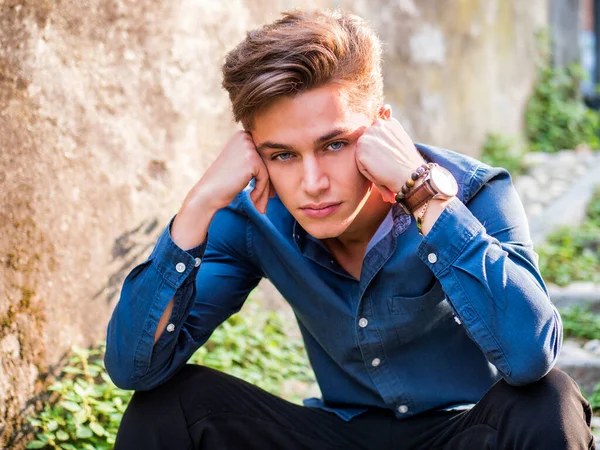 Avrupa 'nın kentsel ortamında oturan yakışıklı, zarif bir genç adam mutsuz, endişeli ya da endişeli bir şekilde kameraya bakıyor.