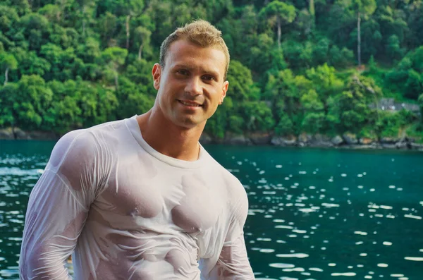 迷人的年轻健美运动员穿着湿衬衫站在海边 面带微笑 看着镜头 — 图库照片
