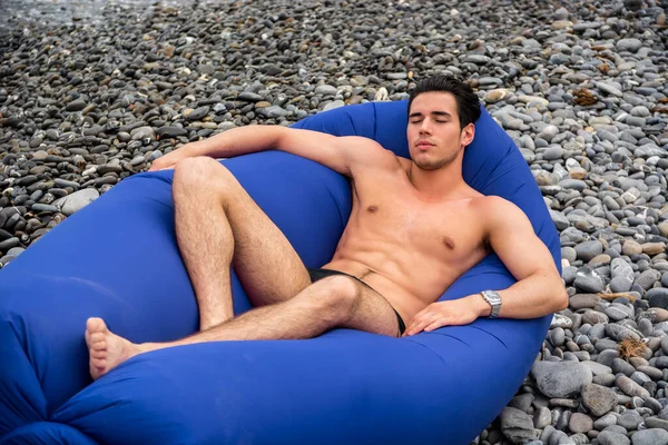 松懈的裸男 双目紧闭 躺在柔软的豆袋上 悠闲地躺在石质海岸上 — 图库照片
