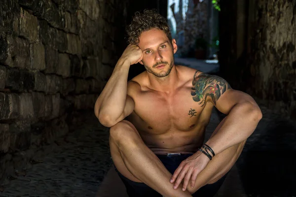 意大利小镇的一条古老的砖巷上坐着一个英俊而健壮的赤身裸体男人 横向室外射击 — 图库照片