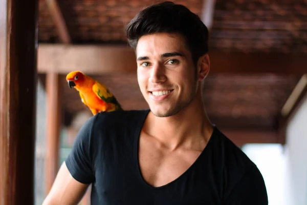 Uśmiechnięty Przystojniak Patrzący Kamerę Papugą Ramieniu Strzał Poziomie Wewnątrz — Zdjęcie stockowe
