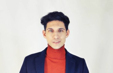 Kırmızı balıkçı yaka kazak ve iş elbisesi giyen yakışıklı genç adam stüdyoda beyaz arka planda poz veriyor, gülümseyerek kameraya bakıyor.