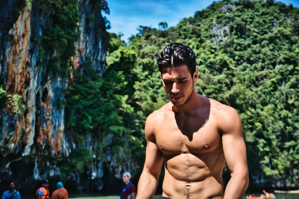 タイのプーケット島のビーチに立っているハンサムな筋肉質の若い男の半分の体のショットは 肩のショートパンツを着て 筋肉質のフィットボディを示し サイドを探して — ストック写真