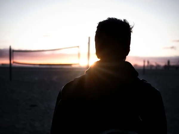 Back view silhouette of male standing against volleyball net and colorful sunset sky in evening time on blurred background