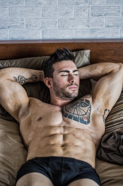 Shirtless muscular sexy male model lying alone on bed in his bedroom, relaxing with eyes closed clipart