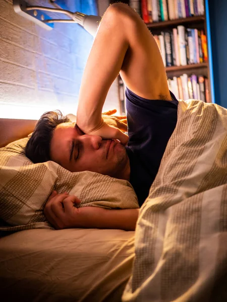 若いハンサムな眠い男 彼は目を覚ますとしてベッドの夜に横たわっている — ストック写真