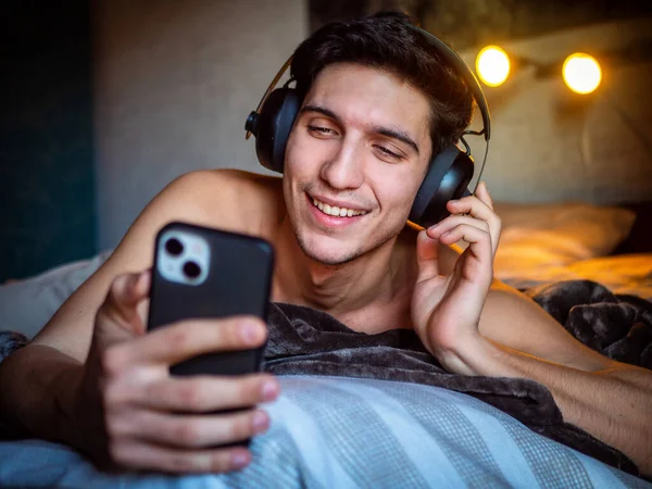 彼のベッドの上に一人で横たわっているヘッドフォンを使用して魅力的な若い男 音楽を聴き 楽しい時間を持っています — ストック写真
