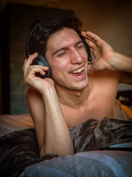 有魅力的年轻人用耳机独自躺在床上 听音乐 玩得很开心 — 图库照片