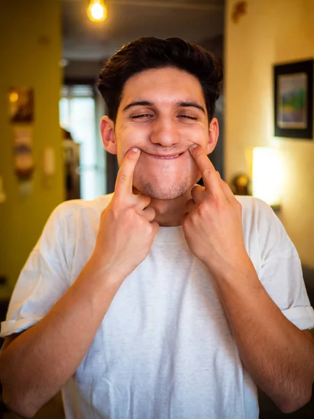 Young Man Forcing His Mouth Smile Pushing His Fingers Indoor — Stock Photo, Image