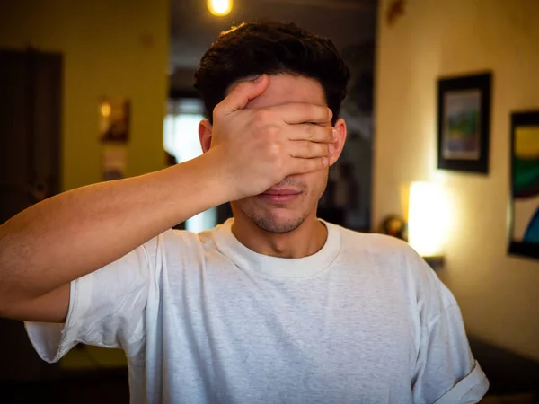Nuori Komea Mies Peittää Silmänsä Kädellään Seisoo Kotona Kasvot Kameraan — kuvapankkivalokuva