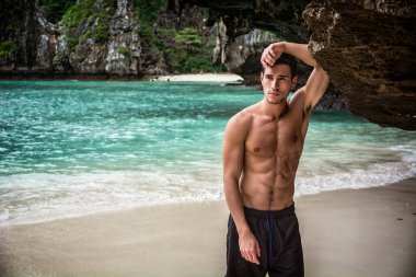 Tayland, Phuket Adası 'nda bir plajda duran çekici genç bir adam. Üstsüz, boxer şort giymiş, kaslı fit bir vücut gösteriyor.