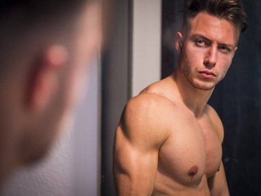Gömleksiz, kaslı, yakışıklı bir adam sabah banyo aynasında kendine bakıyor.