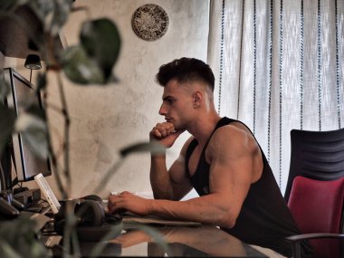 Waist Up Profile of Young Attractive Man with Dark Hair, Sitting at Computer Desk Working on Paper Homework or on His Start-up Business, in Dorm Room