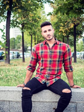 Modern Avrupa şehrinde kot pantolon ve kırmızı kareli gömlek giyen yakışıklı bir genç adam.