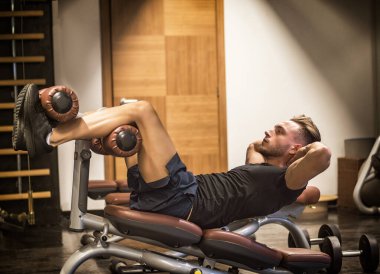 Yakışıklı, kaslı genç bir adam spor aletleri üzerinde bacak egzersizi yapıyor.