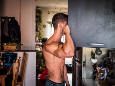 Genç üstsüz vücut geliştirici mutfak dolabında ya da dolapta yiyecek arıyor.