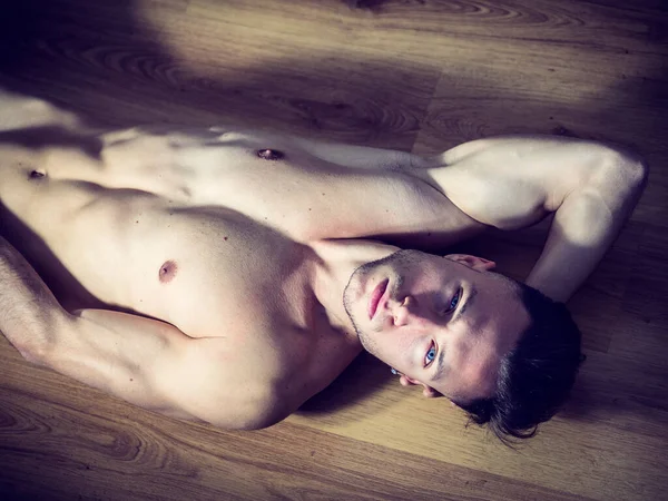 ハンサムな全裸筋肉青年魅惑的な態度で自宅に堅木張りの床の敷設カメラ目線 — ストック写真