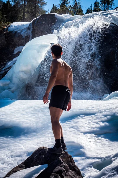 雪の上に立っている国の屋外の筋肉のシャツレスの若い運動選手の背部ショット 山を眺めながら健康な筋肉体を見せる — ストック写真