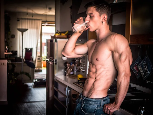 ガラスから水を飲むキッチンに立っている筋肉体を持つ若いシャツレスの男 — ストック写真
